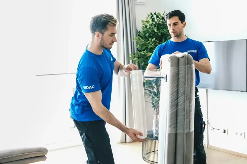 2 Möbelpacker folieren ein Sofa mit durchsichtiger Folie für den Transport.