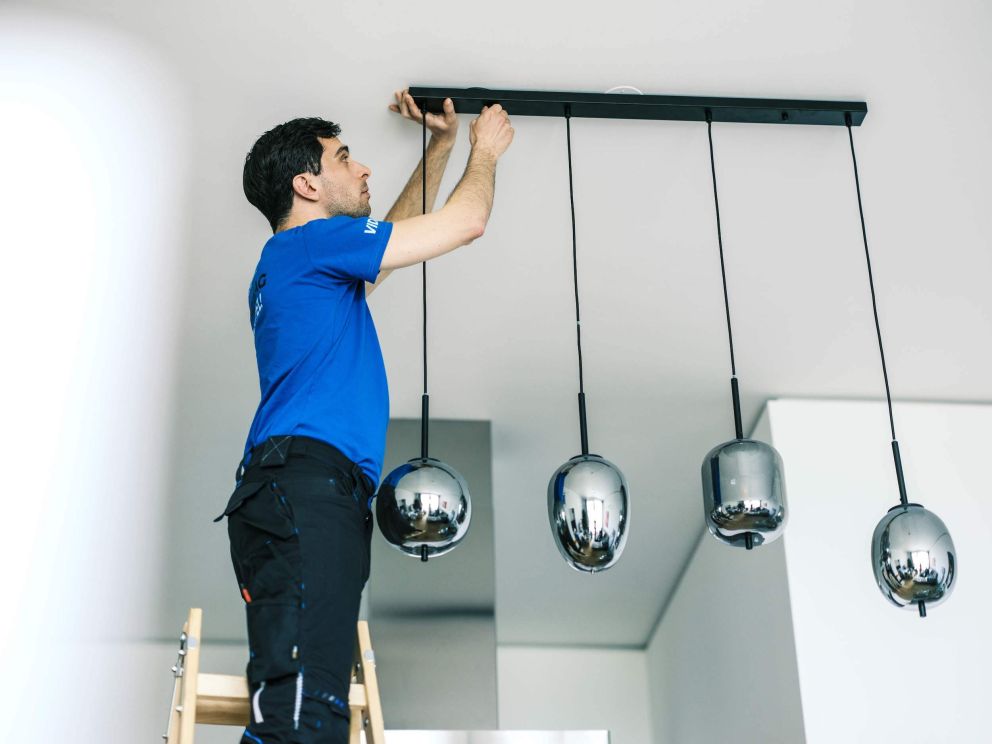Umzugsmonteur montiert Lampe im Esszimmer. DasUmzugsteam.