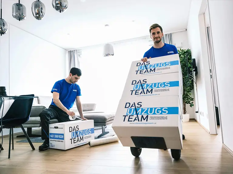 Umzugsservice - 2 Möbelpacker in einer Wohnung und verpacken Gegenstände und fahren sie mit Rollwagen hinaus.