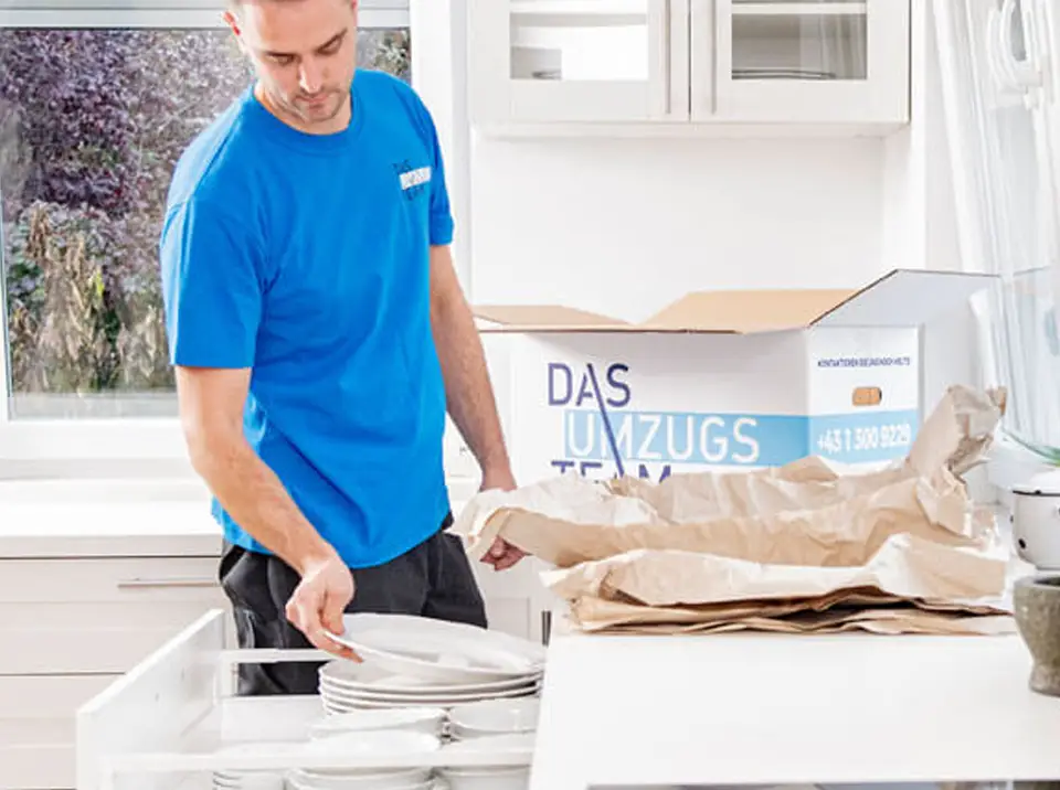 Ein Umzugshefler verpackt Geschirr in einen Karton