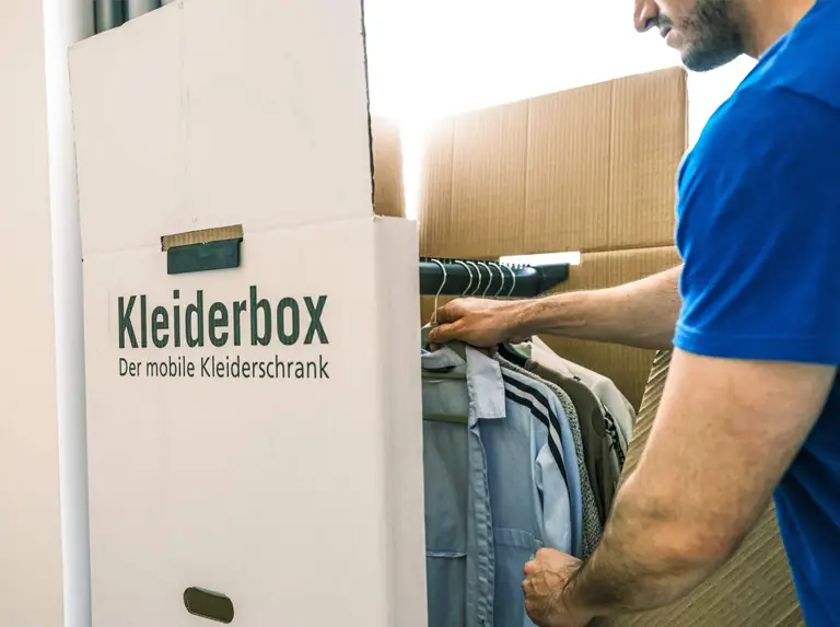Ein Möbelpacker packt einen Kleiderkarton ein