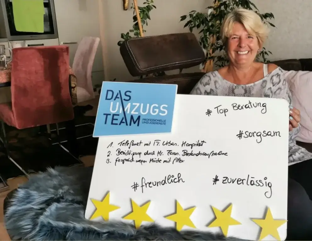 Eine blonde, ältere Dame mit fröhlichem Lächeln sitz auf einem Sofa und hält eine Bewertungstafel von DasUmzugsteam mit 5 goldenen Sternen in der Hand.