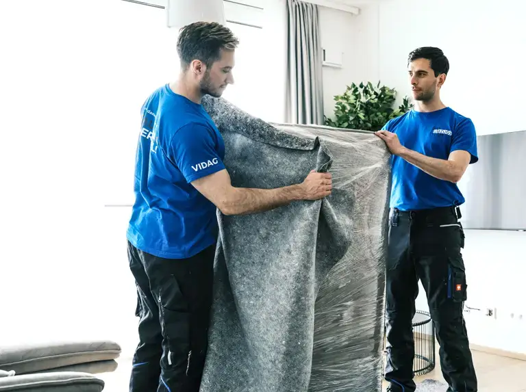 Möbelpacker beim Verpacken eines Wohnzimmerkastens mit Schutzfolie und Umzugsdecke