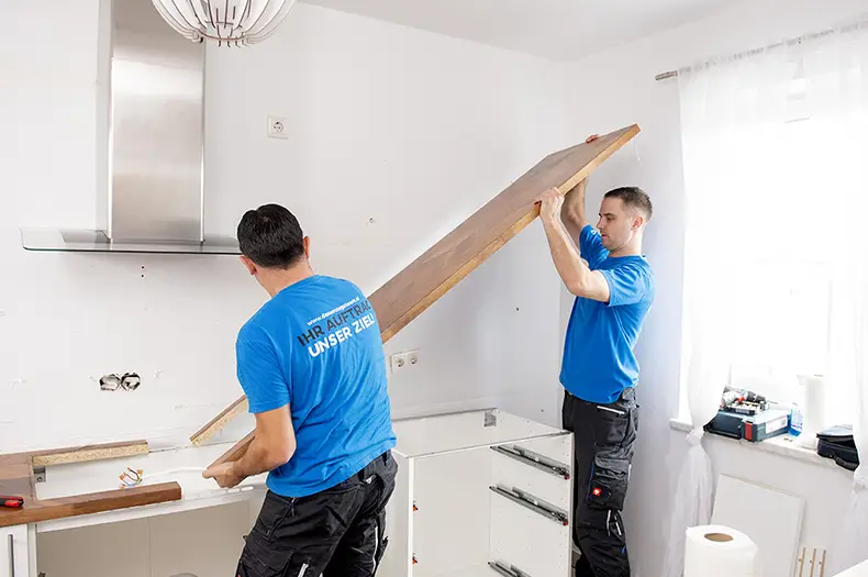 Ikea Küchenmontage: 2 Monteure heben eine Küchenarbeitsplatte auf Unterschränke einer Küche.