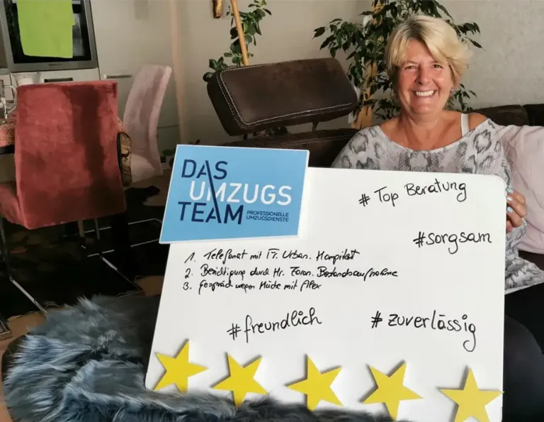 Eine blonde, ältere Dame mit fröhlichem Lächeln sitz auf einem Sofa und hält eine Bewertungstafel von DasUmzugsteam mit 5 goldenen Sternen in der Hand.