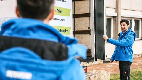 Ein Möbelpacker steht vor einem Umzugs LKW und öffnet Türe