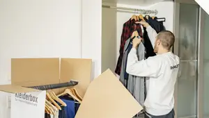 Ein Möbelpacker verpackt Kleider in einen Kleiderkarton