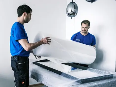 Möbelpacker Wien: 2 Umzugshelfer verpacken einen Spiegel in Folie.