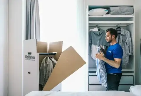 Zusatzleistungen: Ein junger Umzugshelfer verpackt Kleidungsstücke in einen Umzugskarton