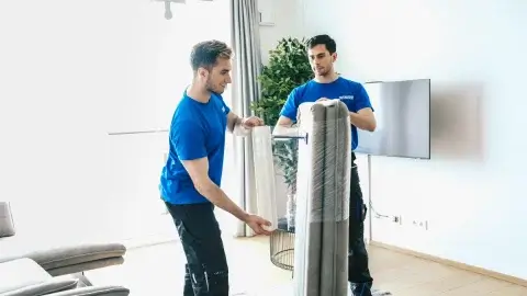 Zwei Möbelpacker folieren ein Sofa